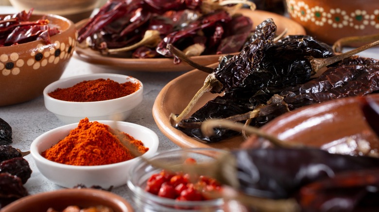 Various dried chile peppers and spices in bowls