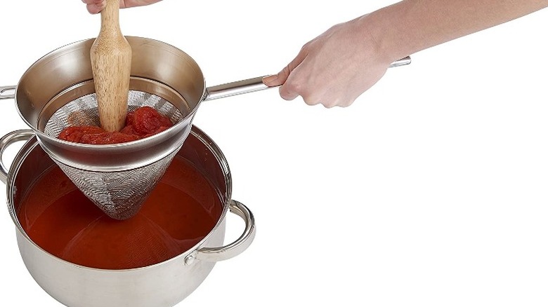 Tomatoes being strained through a chinois