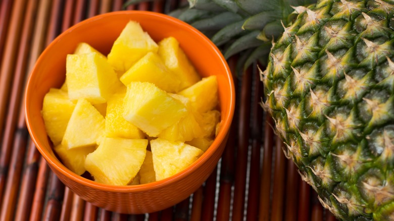 A bowl of pineapple chunks next to a pineapple