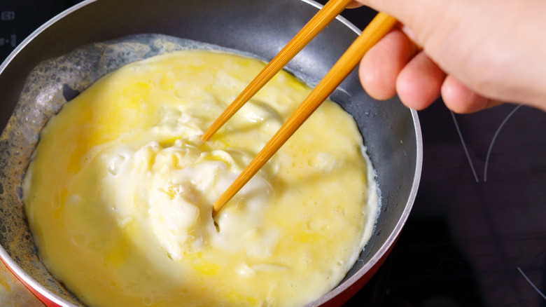 Hand using chopsticks to cook an omelet