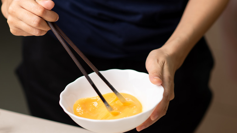 Person's hands scrambling eggs with chopsticks