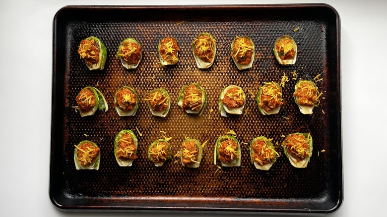 chorizo-stuffed brussels sprouts on a baking sheet topped with shredded cheddar