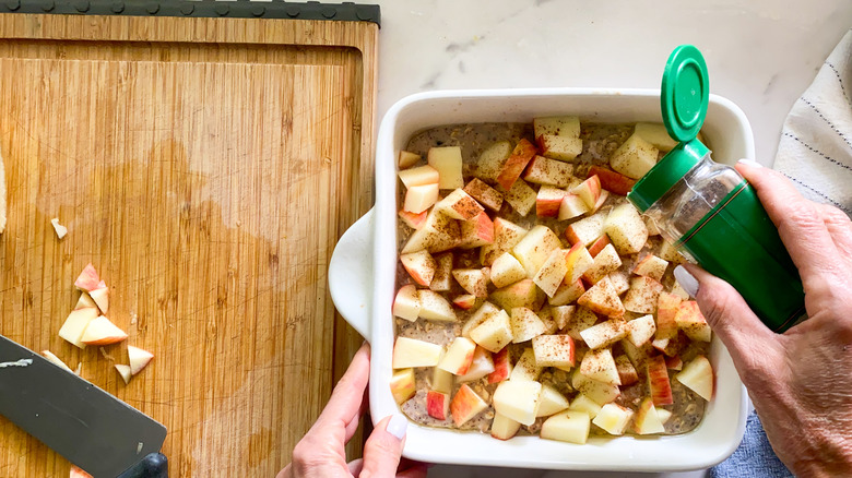 sprinkling cinnamon on apples in oatmeal dish