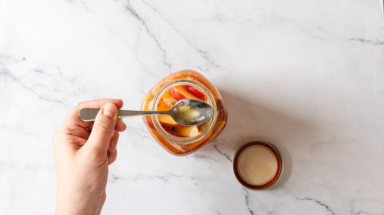 Hand holding a spoon with kombucha over jar