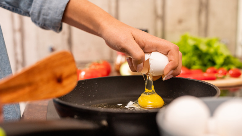 a person cracking an egg into a skillet