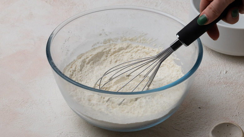 glass bowl containing flour and whisk