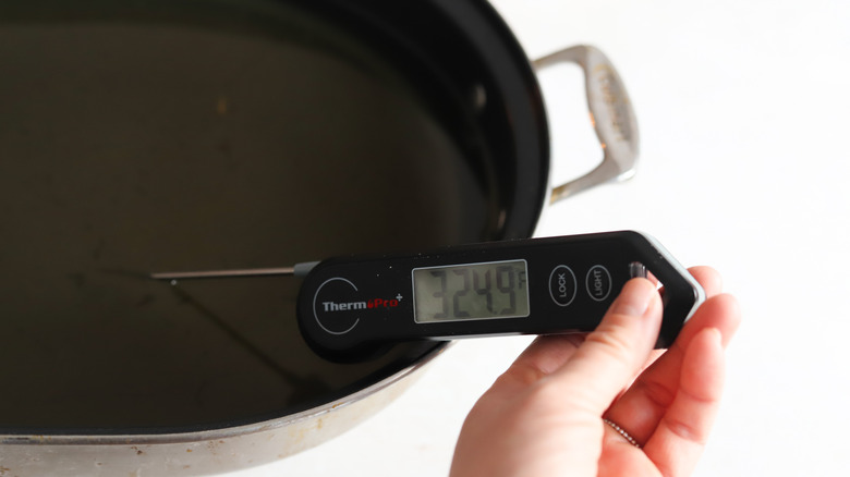 vegetable oil heating in a pan, hand holding meat thermometer