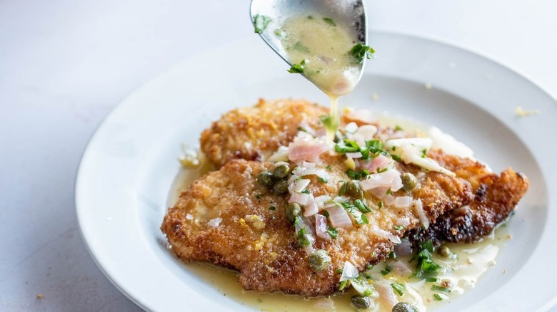 spoon pouring piccata sauce over breaded chicken