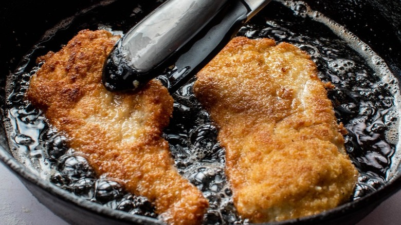 tongs flipping fried chicken in hot oil 