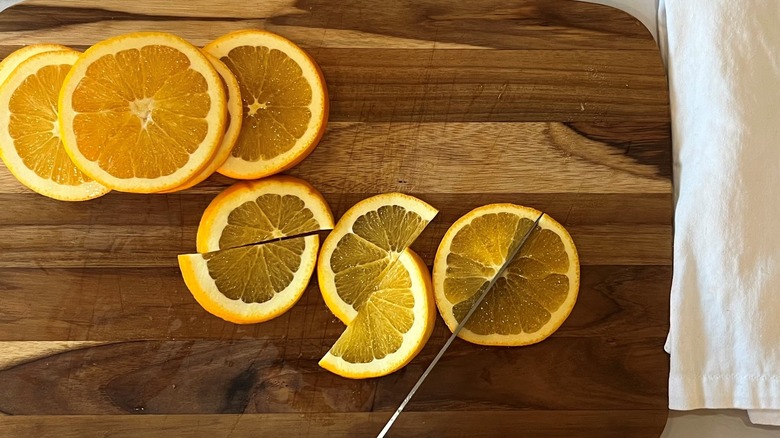 Knife slicing orange on wooden board