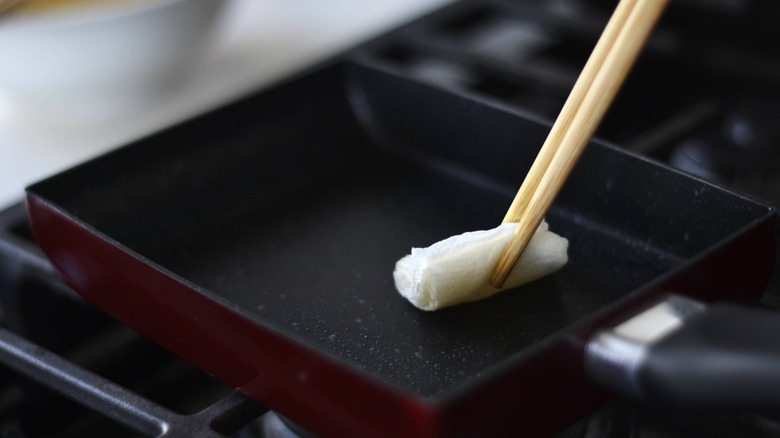 chopsticks greasing pan with rolled-up paper towel