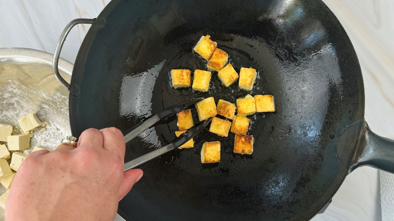 hand stirring tofu in pan