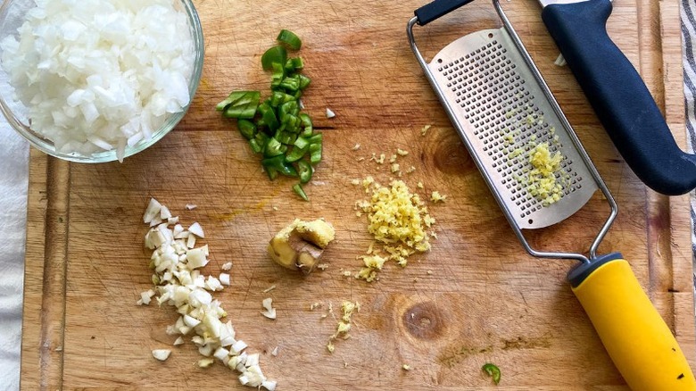 cutting board with chopped onion, green chili, minced garlic, and grated ginger