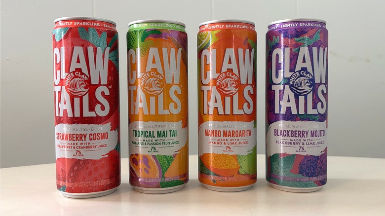 Four White Claw ClawTails cans lined up on a white table