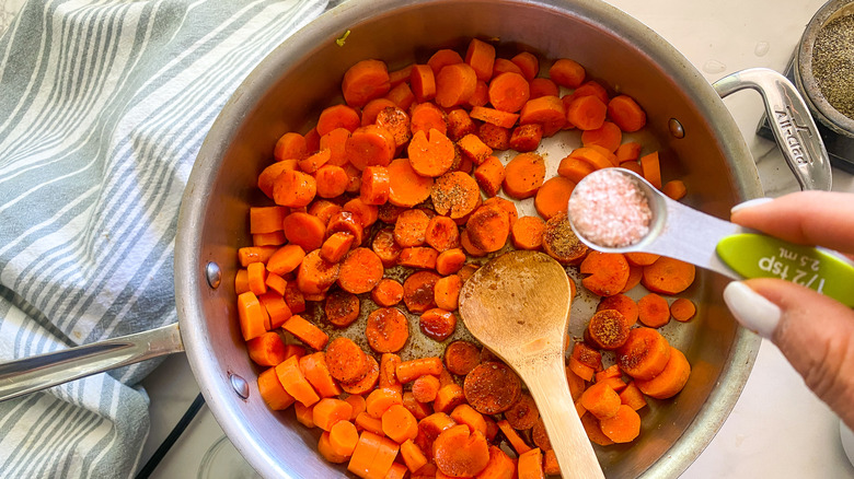 adding salt to carrots in pan