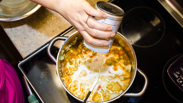 pouring coconut milk into pot of beans