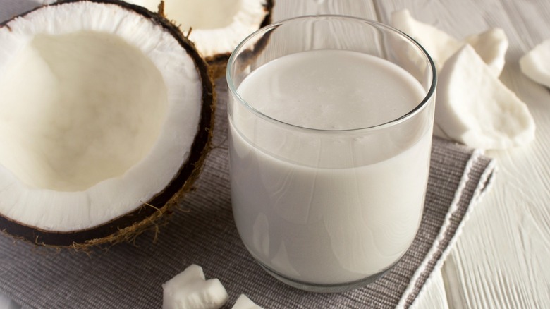 Glass of coconut milk beside a halved coconut