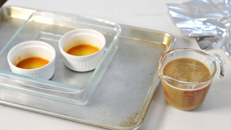 Two ramekins filled with caramel sauce and a measuring cup of custard mixture
