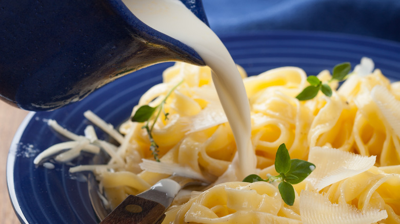 Pouring alfredo sauce onto pasta