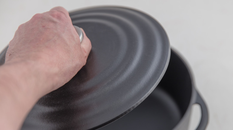 hand putting a lid on a cast iron pot