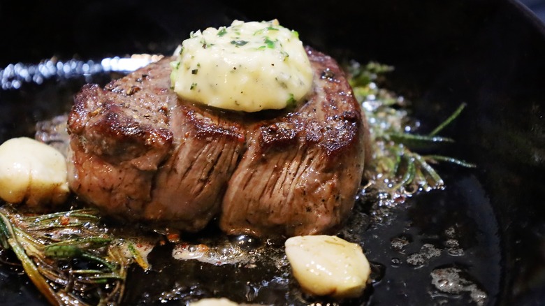 searing steak in a cast iron pan with butter and herbs