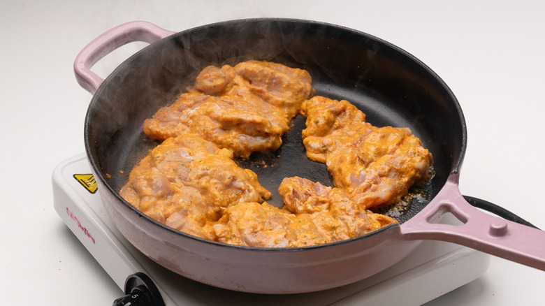 Marinated chicken thighs cooking in pan