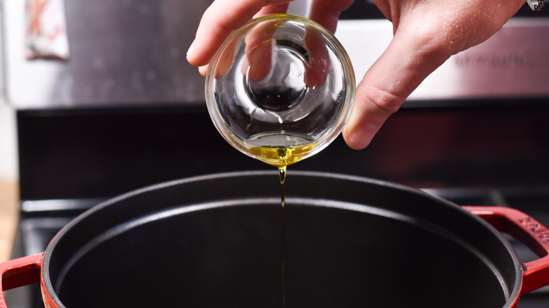 hand adding olive oil to pot