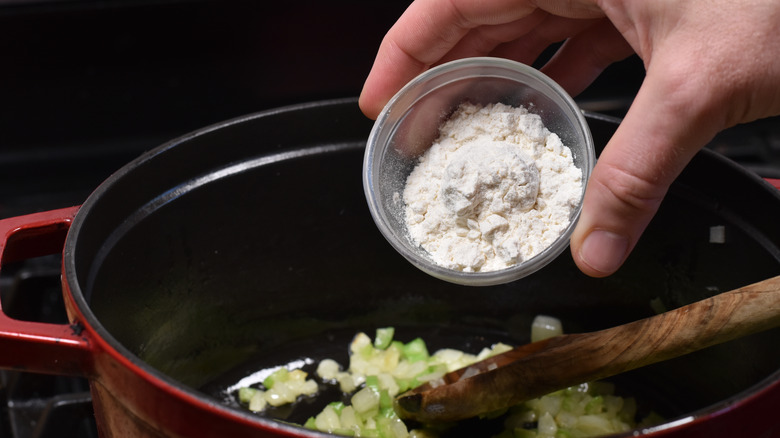 hand adding flour to vegetables in soup pot