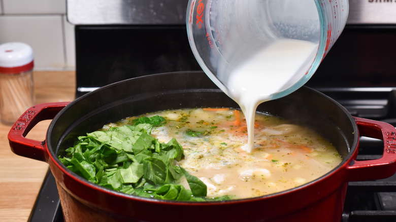 adding cream to vegetable soup in pot