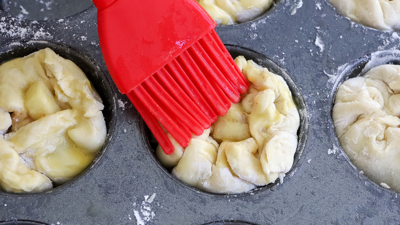 red brush painting the surface of dough in a muffin cup