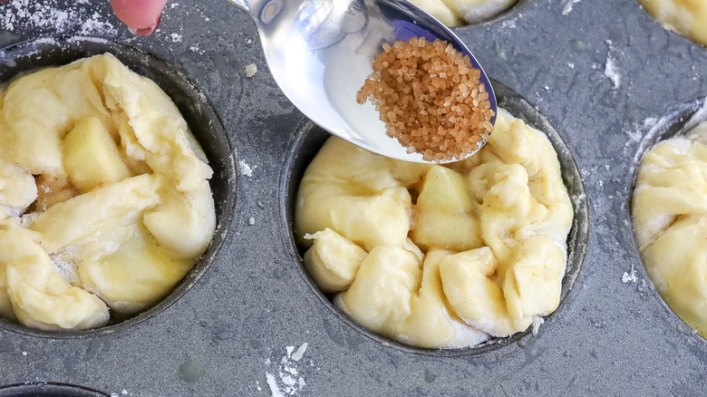 hand sprinkling brown sugar over a muffin pan full of dough