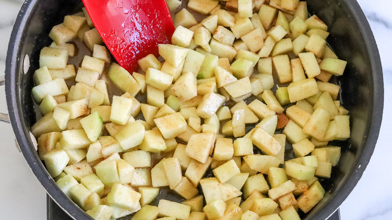 apple chunks in a black frying pan with a red spatula