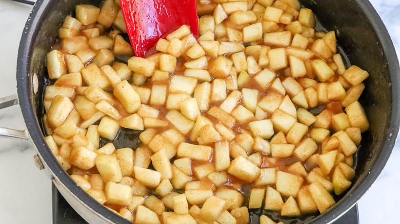 cooked apple chunks in a black frying pan with a red spatula