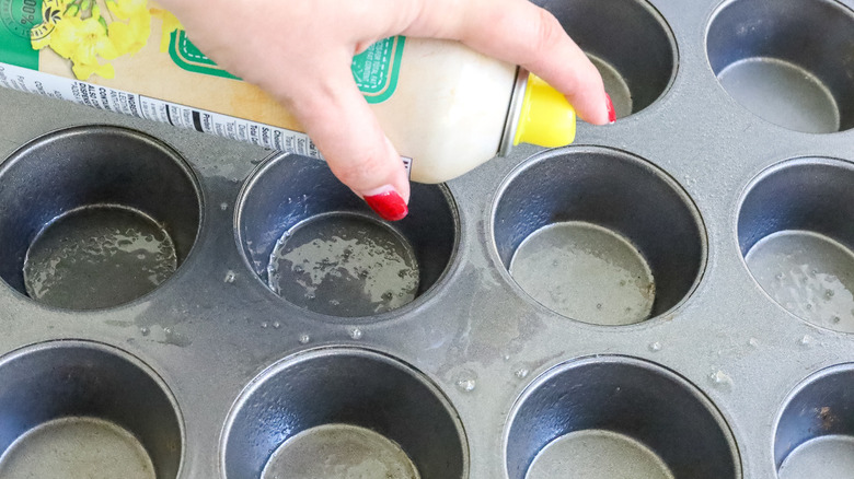 hand squirting cooking spray on a muffin pan