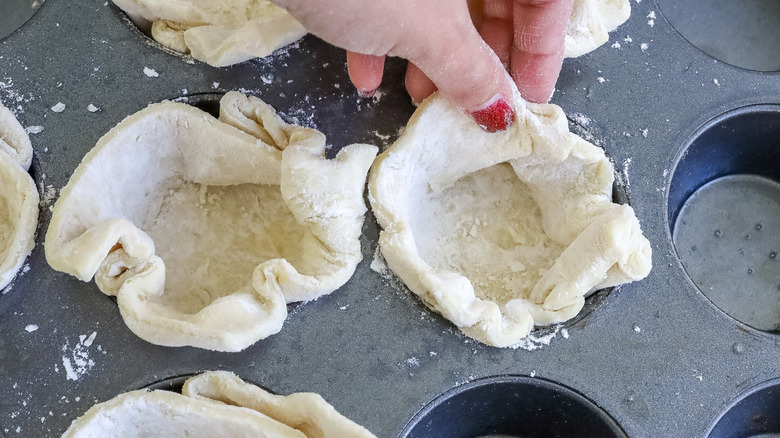 hand pressing dough into muffin cups