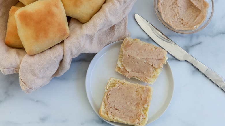 A roll cut open on a plate with cinnamon butter spread on it