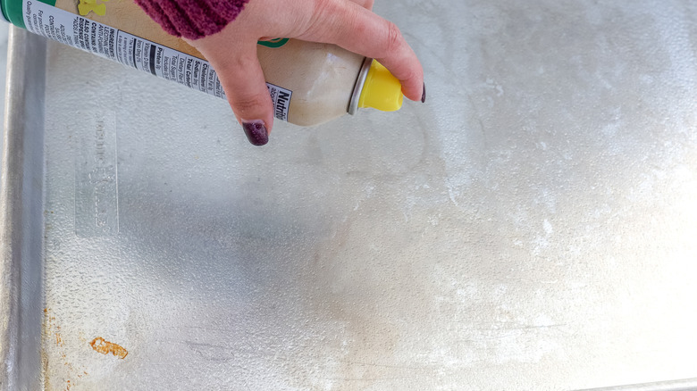 A hand spraying baking sheets with cooking spray