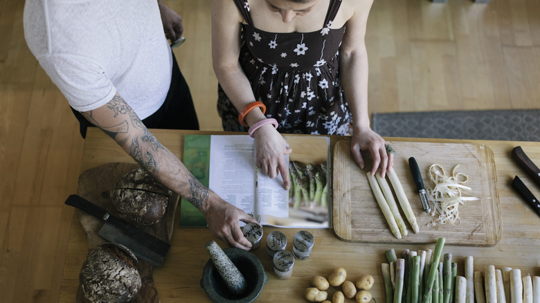 Overhead view of couple cooking with cookbook