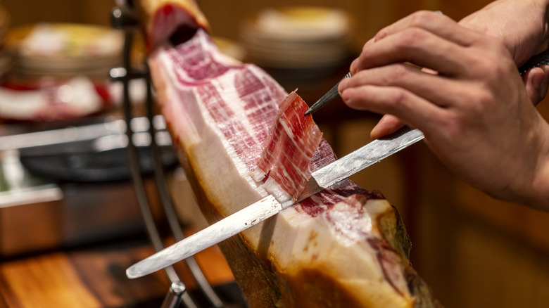 Hands carving serrano ham on a stand