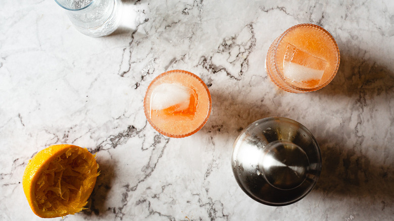 two glasses of orange drink beside soda and shaker