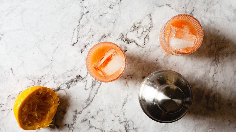 two glasses of orange drink beside shaker and orange peel