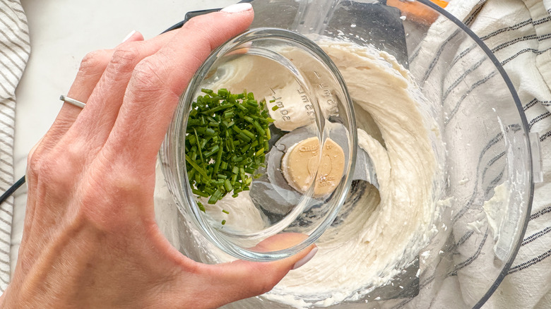 hand adding chives to processor