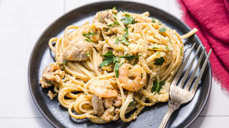 Serving of pasta, chicken, sausage, and shrimp in cream sauce with Parmesan and parsley