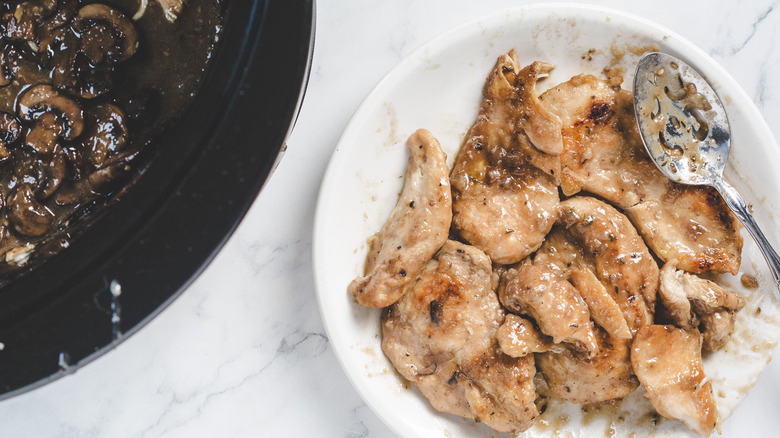 Chicken on plate beside crockpot