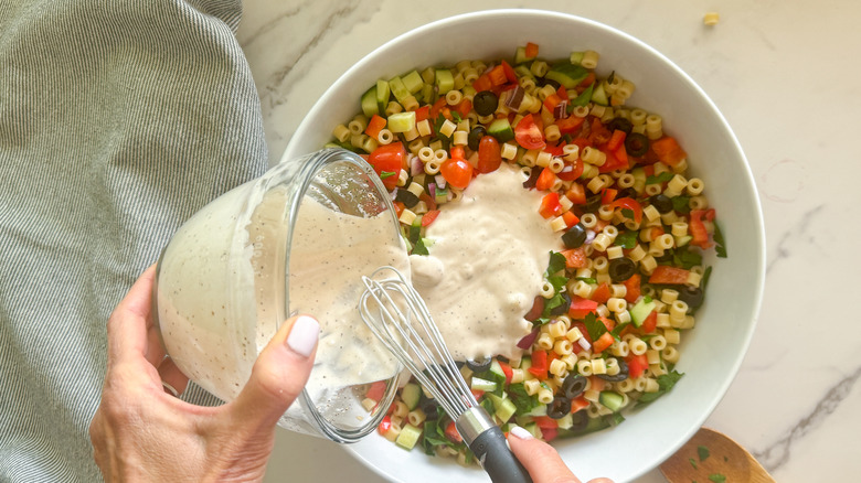 hand adding dressing to salad