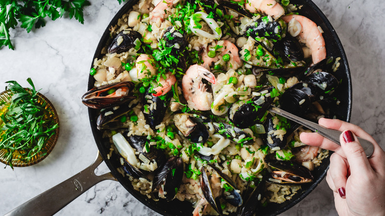 Hand serving risotto from a large pan