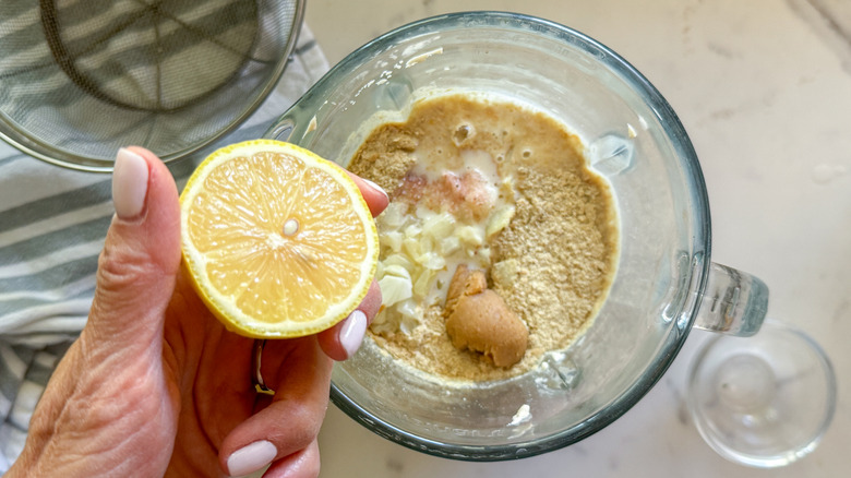 Hand holding half of a lemon over a blender of sauce