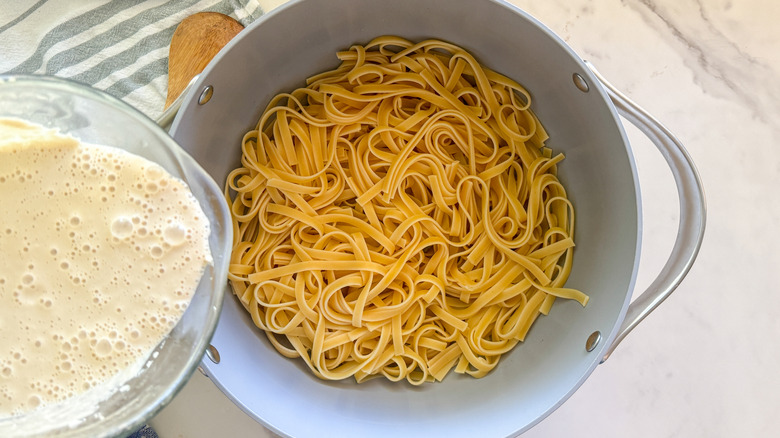 Container of sauce over pot of cooked pasta