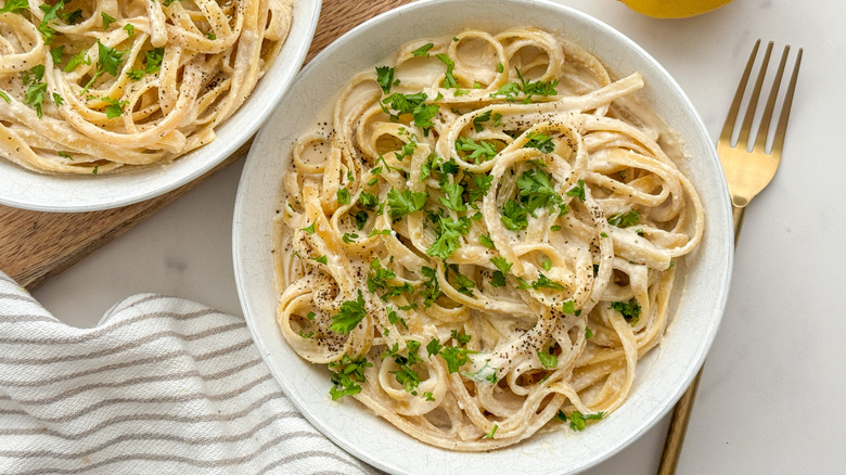 Two bowls of pasta with a tea towel and gold fork