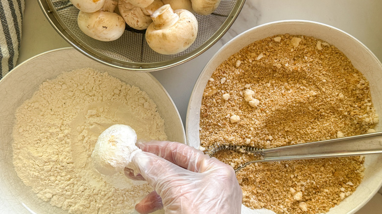 hand dipping mushroom into flour